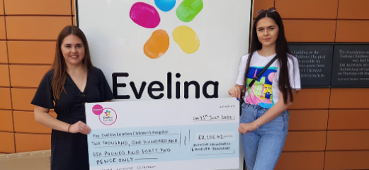 Amelia and her friend outside the Evelina London sign with a large cheque