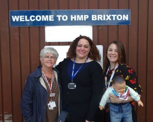 A group of professionals from Evelina London beside a sign that reads &amp;quot;Welcome to HMP Brixton&amp;quot; and a doll which is used in training.