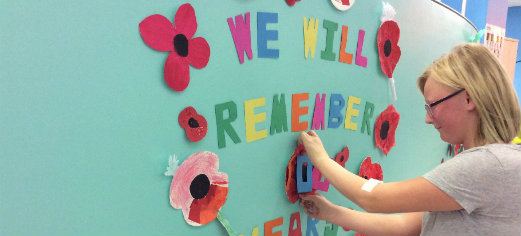 Tilly making adding paper poppies to a display for rememberance day that reads we will remember.